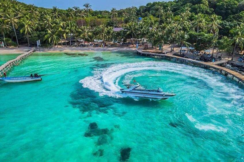 A boat creating a wake in turquoise water, surrounded by a beach with palm trees and a pier. 5