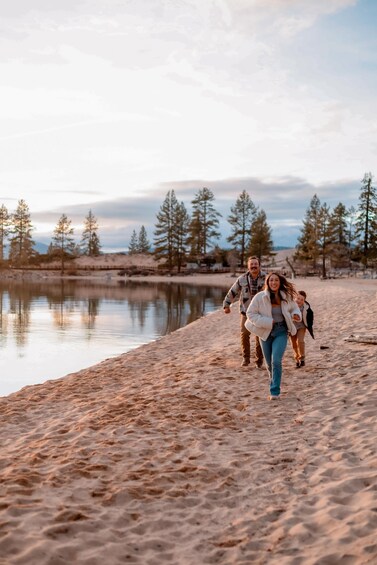 A family walking along a sandy beach with a lake and trees in the background. 1