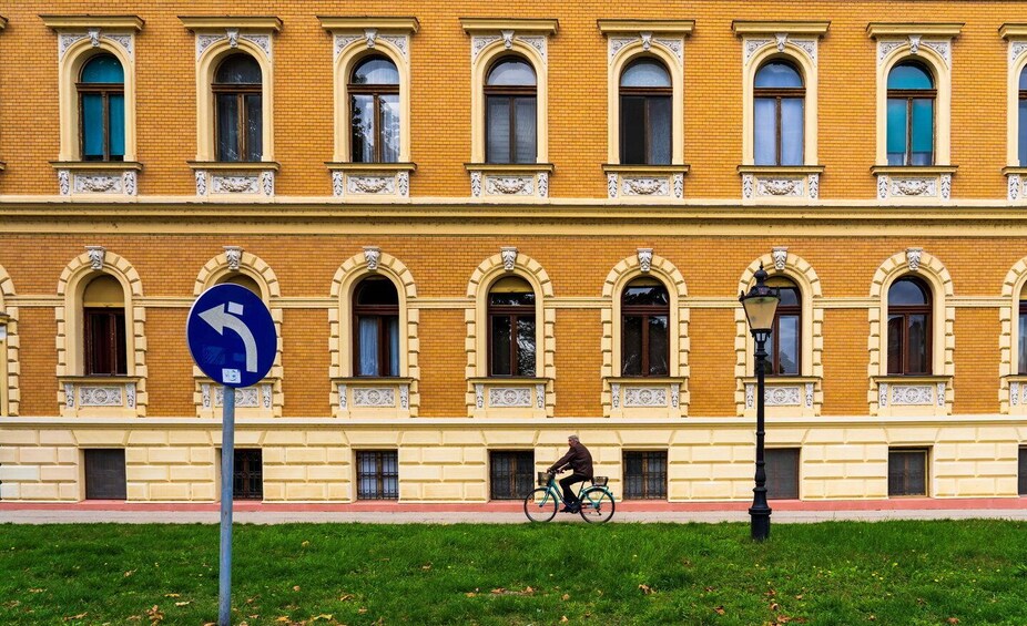 A yellow brick building with arched windows and a cyclist riding past. 3