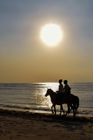 Two people riding horses on a beach at sunset. 4