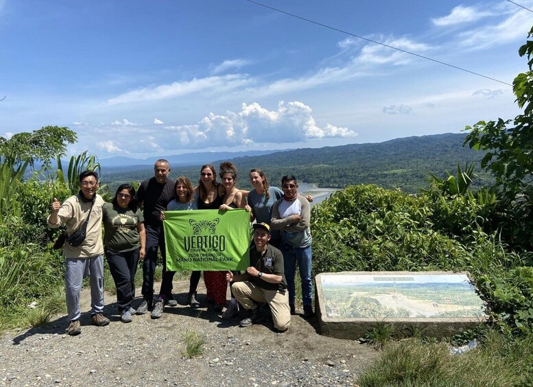 A group of people posing with a banner at a scenic viewpoint overlooking a valley. 1