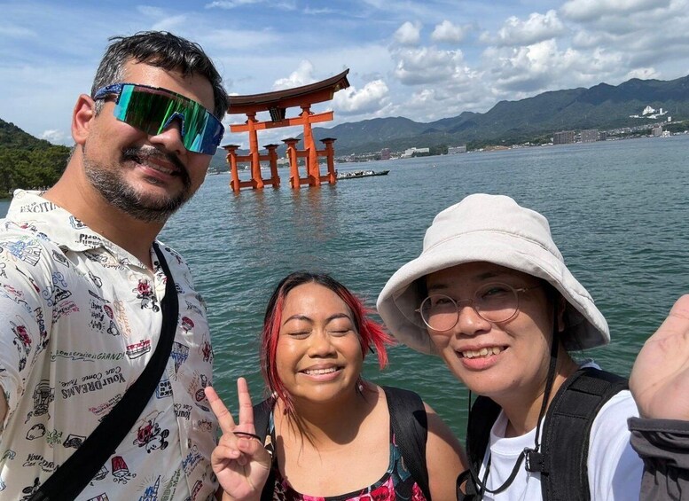 A group of people near a torii gate over water with mountains in the background. 2