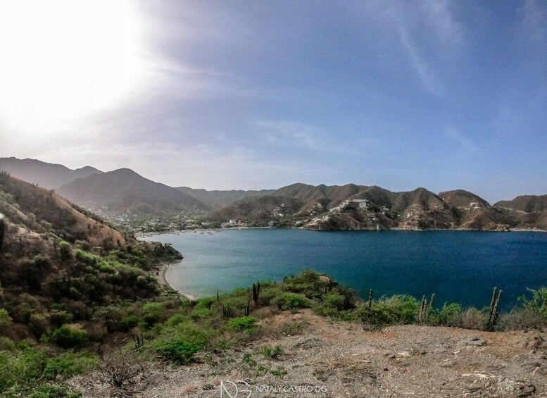 A coastal landscape with a clear blue lake, hills, and sparse vegetation. 5
