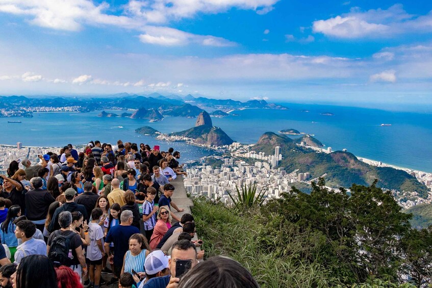 A crowded viewpoint overlooking a coastal city with a prominent mountain peak. 5