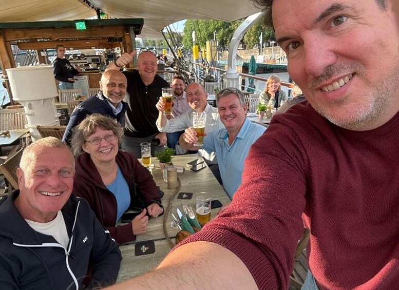 A group of people at an outdoor dining area with tables and chairs, a bar counter, and a view of a body of water in the background. 2
