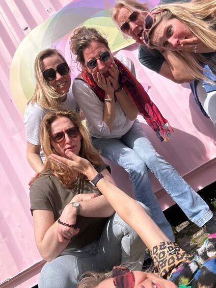 A group of people sitting on a pink surface with a colorful mural in the background. 1