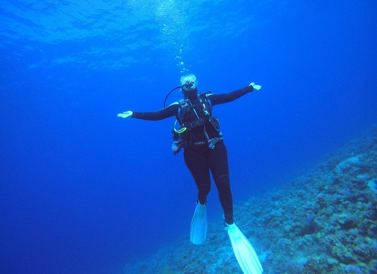 A diver with arms outstretched, wearing fins and a scuba tank, underwater. 3