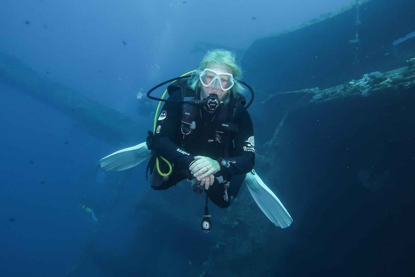 A diver in a black wetsuit with fins, holding a camera, underwater. 1
