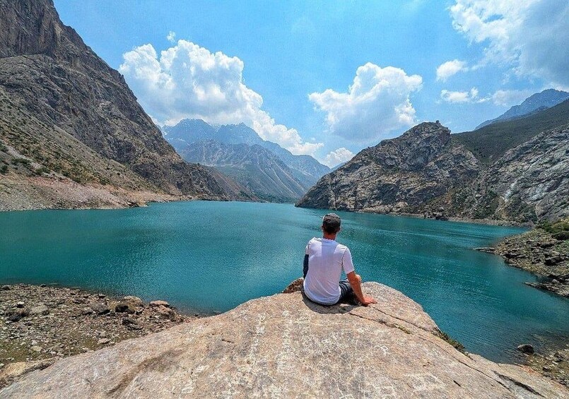 A person sitting on a rock by a turquoise lake surrounded by mountains. 1