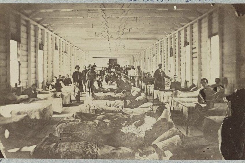 Una habitación amplia y poco iluminada con filas de camas y gente acostada, que sugiere un hospital o centro médico. 1