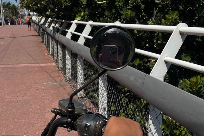 Eine Person fährt Motorrad, eine Kamera ist am Lenker befestigt, im Hintergrund ist ein Drahtzaun und viel Grünwerk zu sehen. 3
