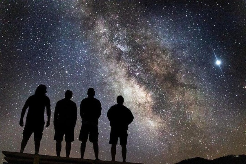 Silhouettes of people standing under a starry night sky with the Milky Way visible. 1