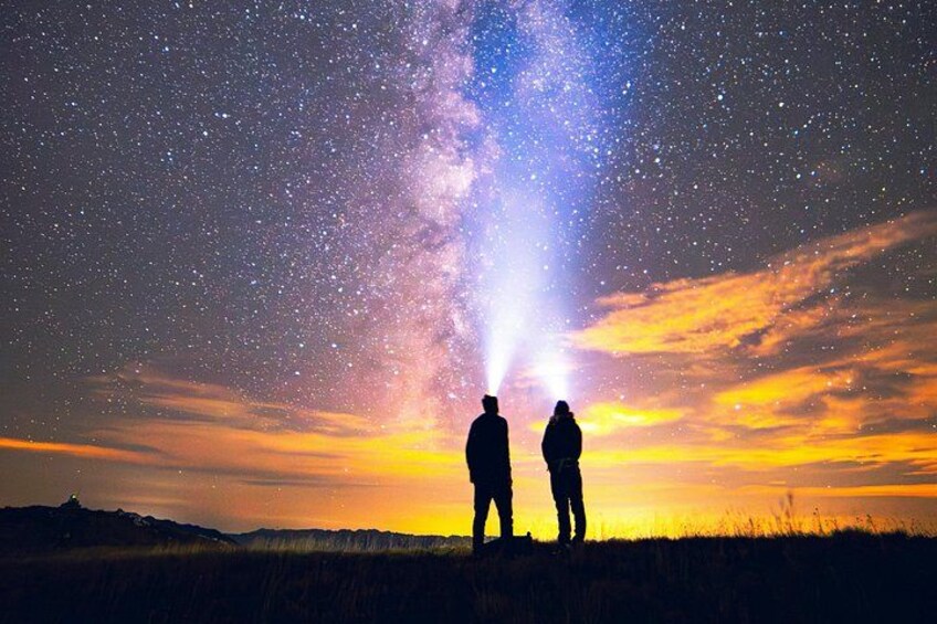 Two silhouettes of people standing on a hill, gazing at a starry night sky with a visible Milky Way. 2