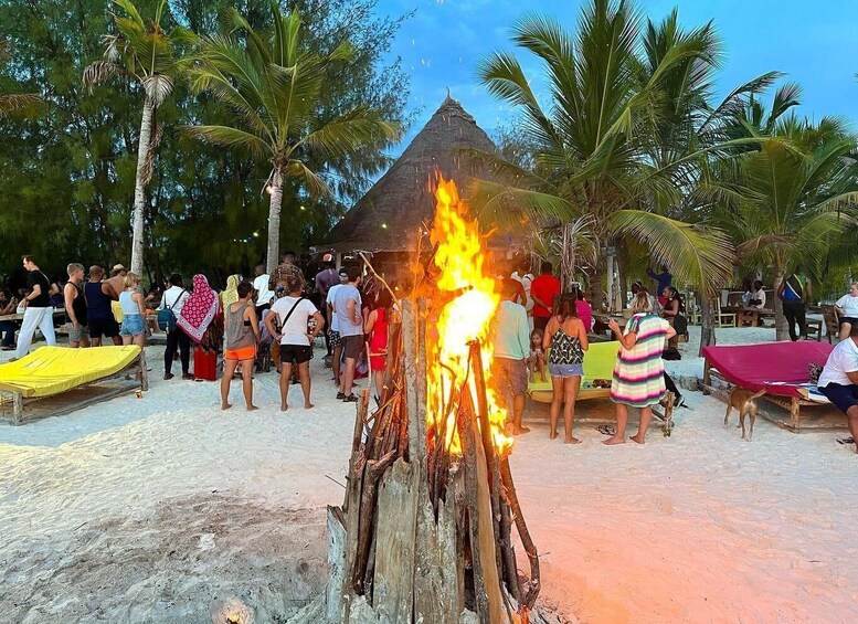 A beach with a fire in the center, palm trees, and people around. 3