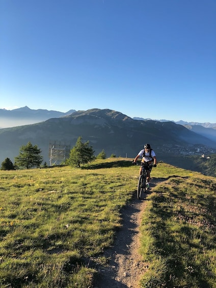 A person riding a mountain bike on a dirt trail with a mountainous landscape in the background. 5