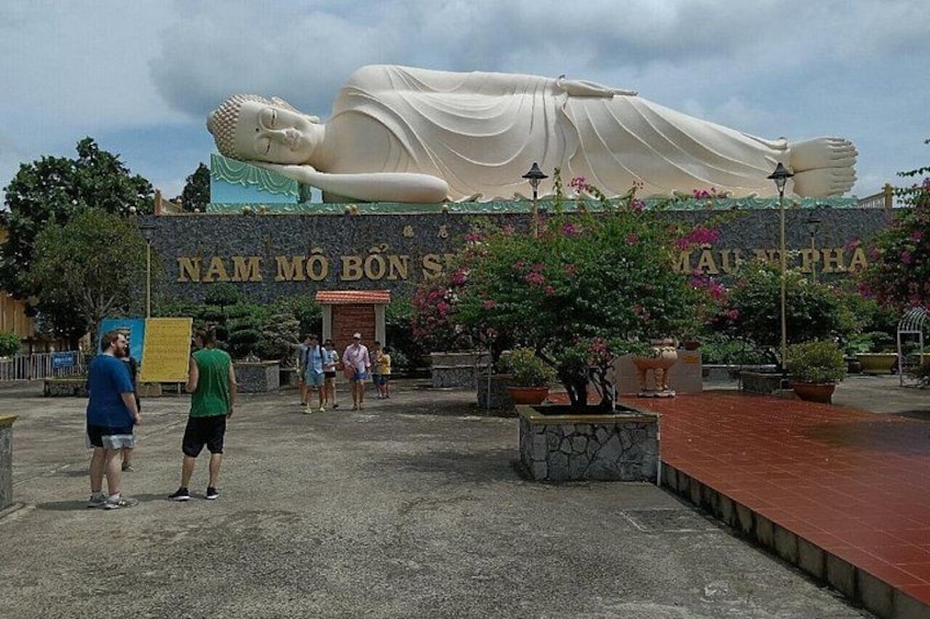 A large reclining Buddha statue, a sign with text, and potted plants. 3