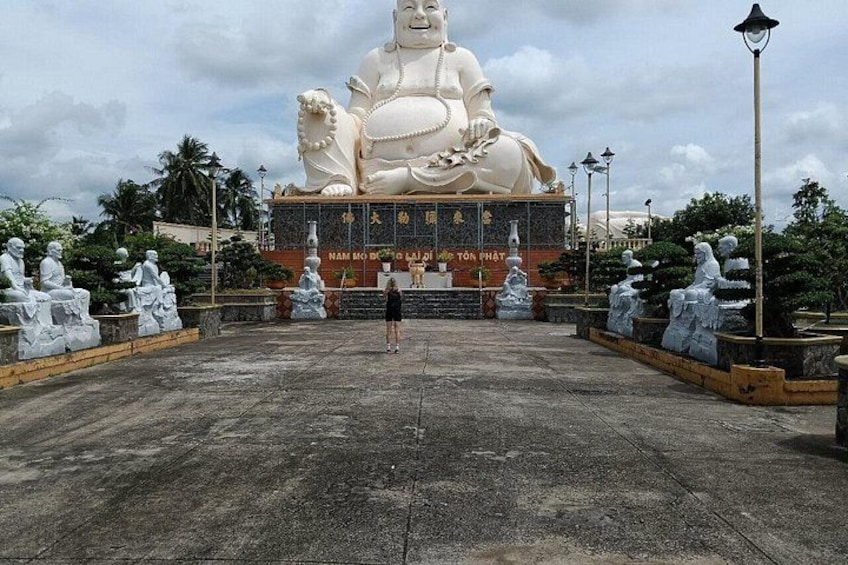 A large white statue of a seated figure with a golden base, surrounded by smaller statues and a paved area. 2