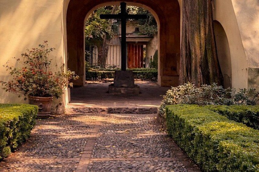 Un sendero adoquinado que lleva a una cruz, rodeado de vegetación y una estructura con arco. 3