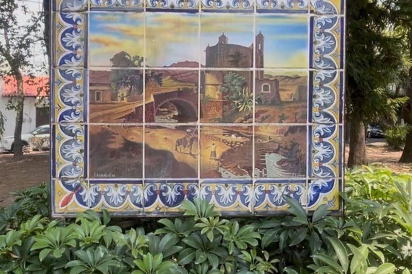 Un mural de azulejos con un puente, edificios y vegetación. 2
