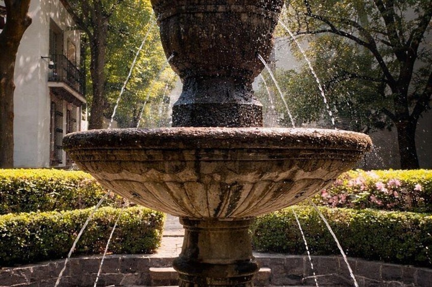 Una fuente de piedra con chorros de agua en un jardín ajardinado con setos recortados y árboles. 5