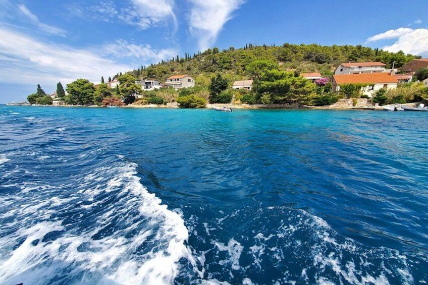 A coastal landscape with a clear blue sea, a small island with houses, and a hilly backdrop. 2