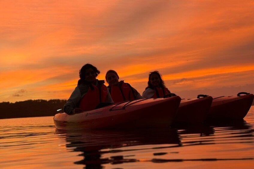 Tre persone in un kayak rosso su un'acqua calma al tramonto. 5