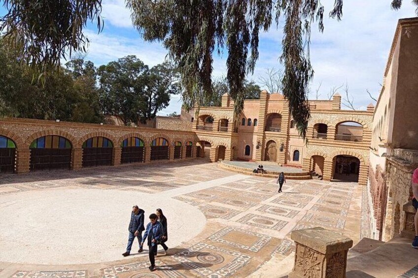 A courtyard with patterned flooring, arches, and a building with arched windows. 1