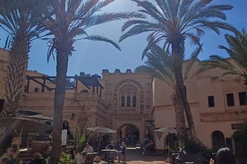 A courtyard with palm trees, a building with arches, and people sitting at tables. 5