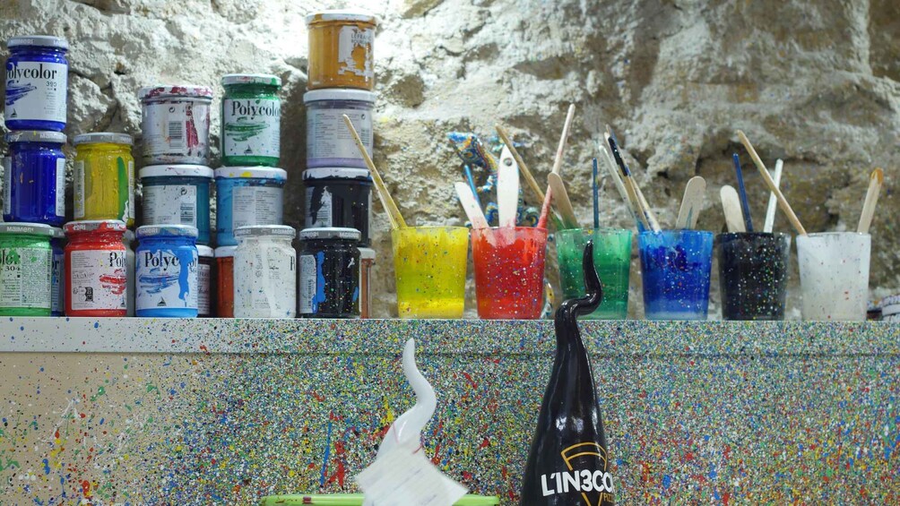 A variety of paint jars and brushes against a textured wall. 1