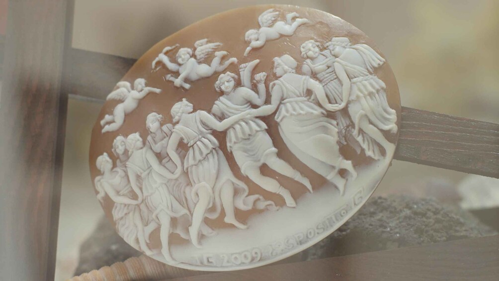 A detailed white relief sculpture on a circular base, depicting a mythological scene with figures and cherubs. 2