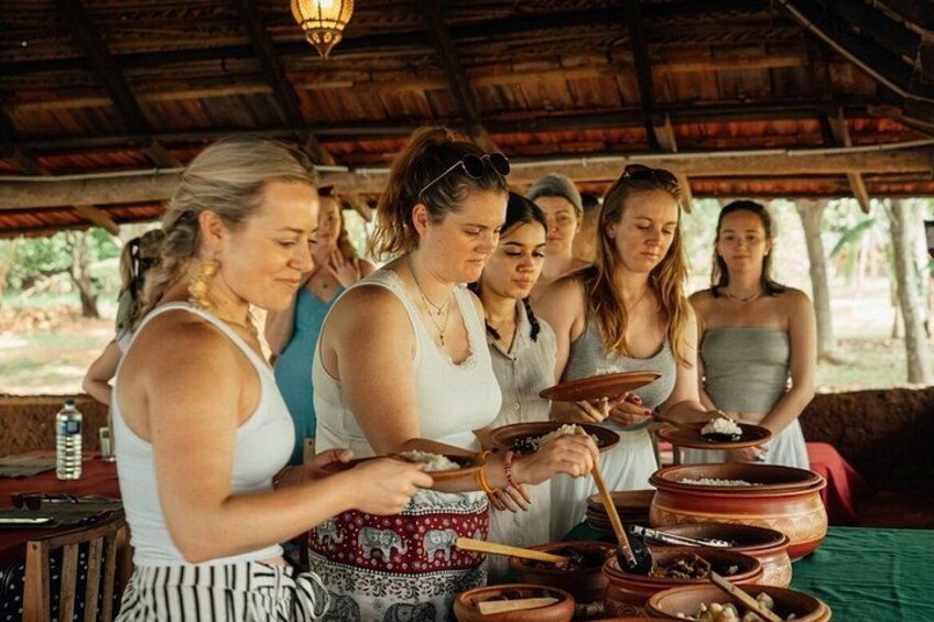A group of people cooking outdoors under a wooden roof. 1