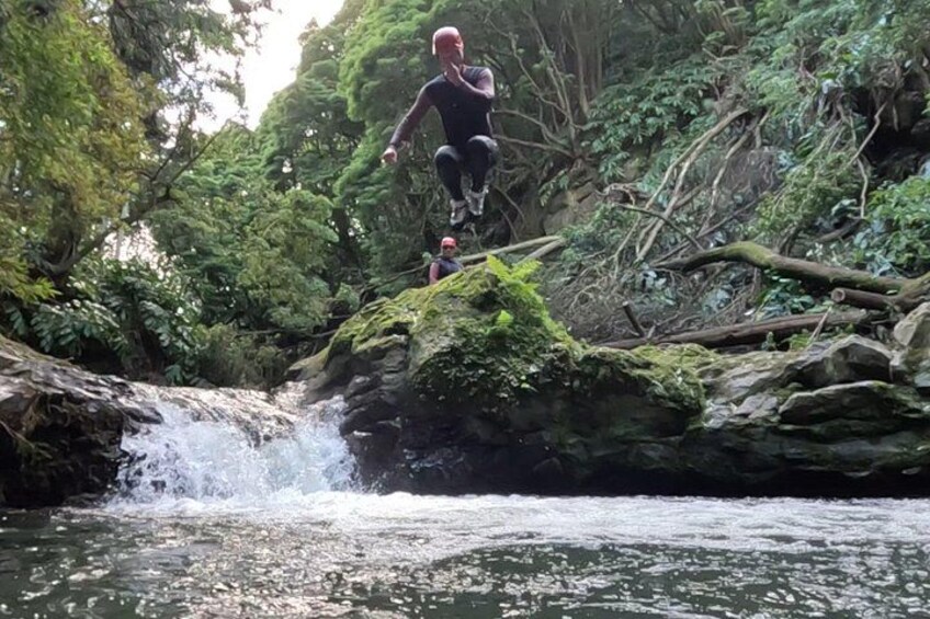 A person jumping over a small waterfall in a forested area. 4
