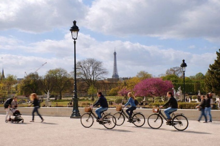 People riding bicycles in a park with a statue and the Eiffel Tower in the background. 1
