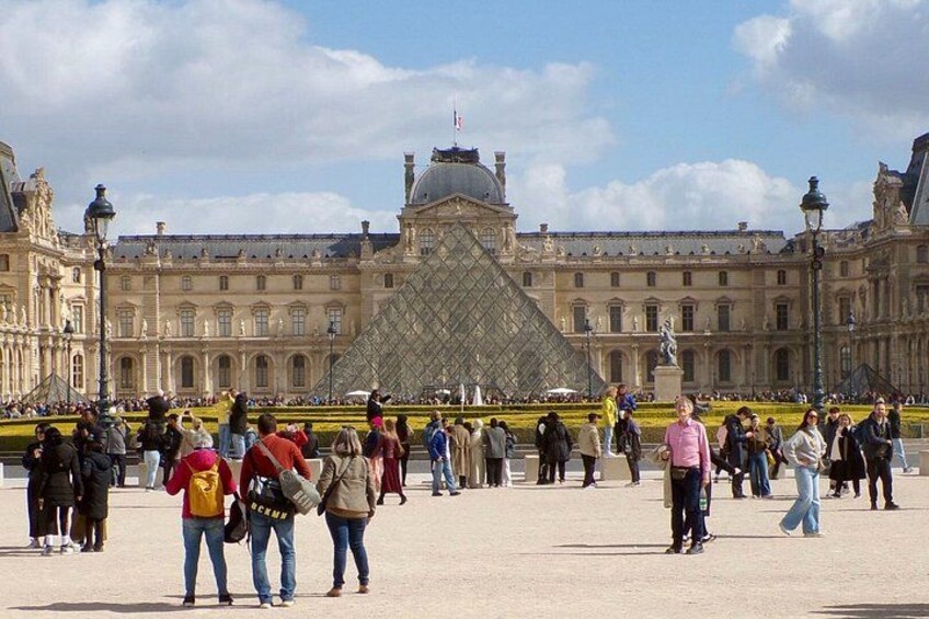 The Louvre Museum with the iconic glass pyramid in the center, surrounded by tourists. 4