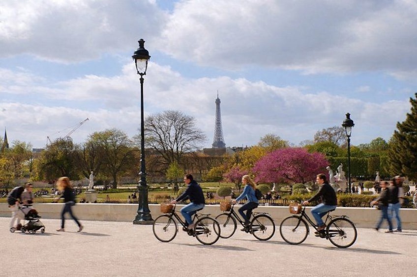 People riding bicycles in a park with a statue and the Eiffel Tower in the background. 1