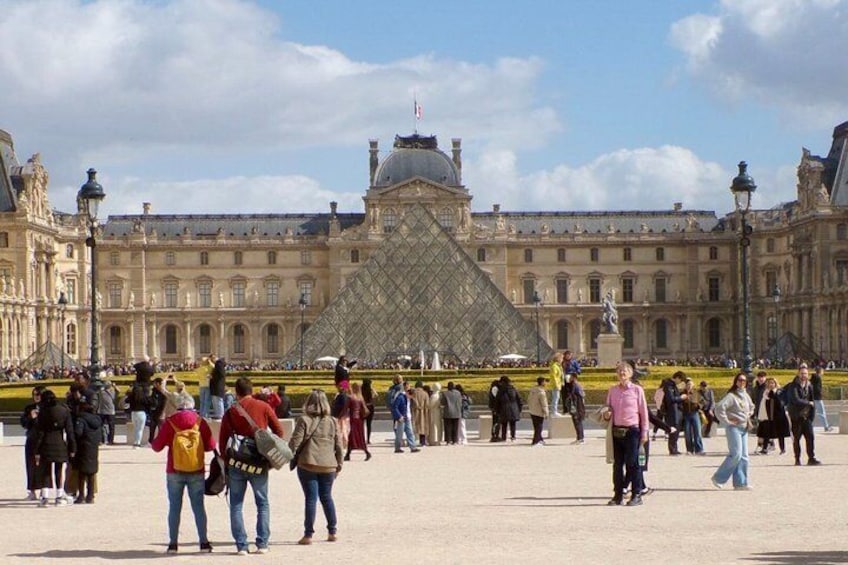 The Louvre Museum's courtyard with visitors, the iconic glass pyramid, and classical architecture. 4