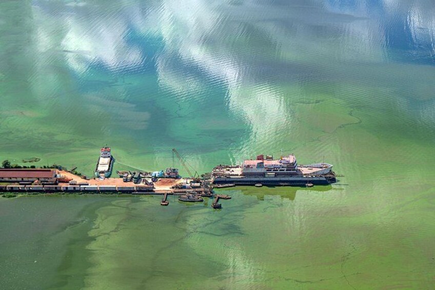 An aerial view of a port with a large ship docked, surrounded by greenish water. 3