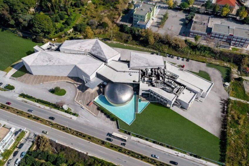 An aerial view of a modern building with a unique spherical structure, surrounded by greenery and a parking area. 3