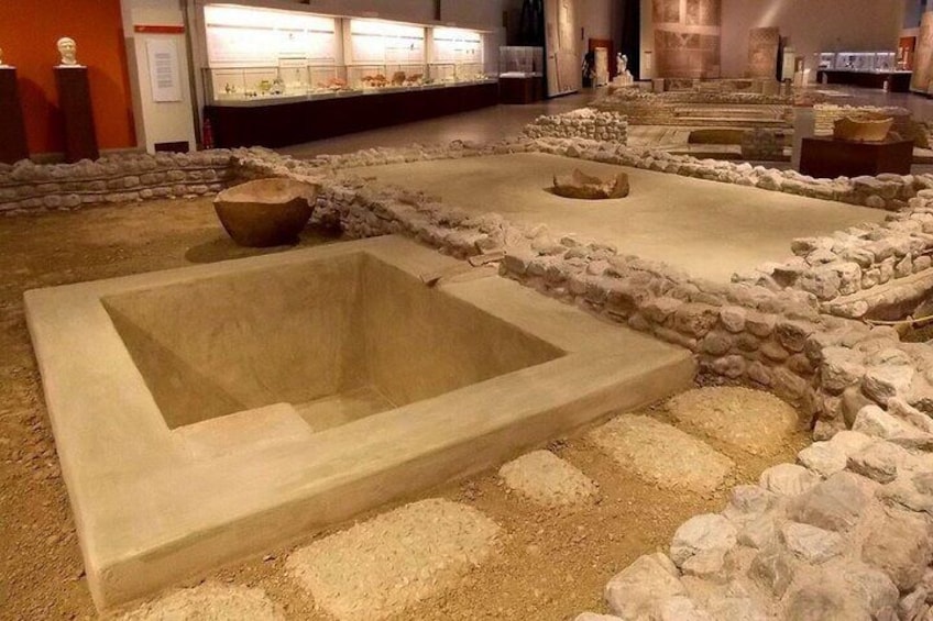 An archaeological site with stone structures and a central rectangular pit. 4