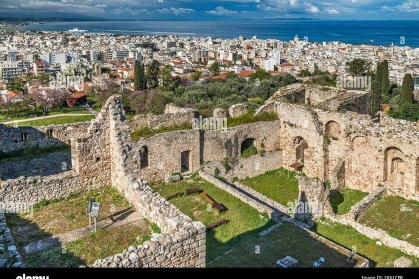 An ancient stone structure with arches and ruins amidst a cityscape with buildings and a coastline. 5