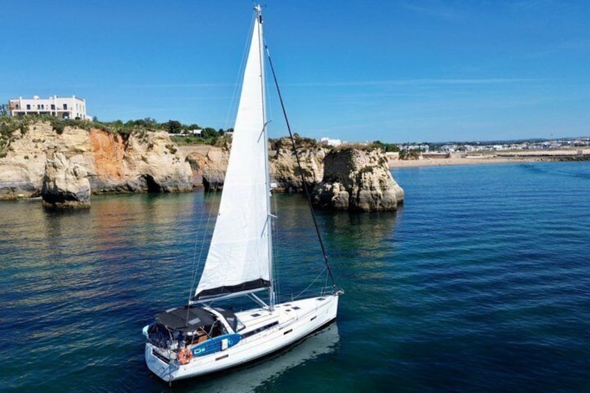 A sailboat on calm waters near rocky cliffs and a white building. 4