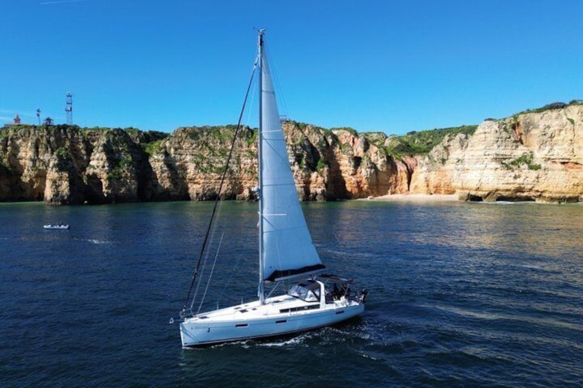 A sailboat on calm waters with cliffs in the background. 1
