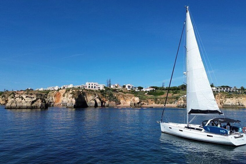 Un velero en aguas tranquilas con un litoral rocoso y edificios al fondo. 5
