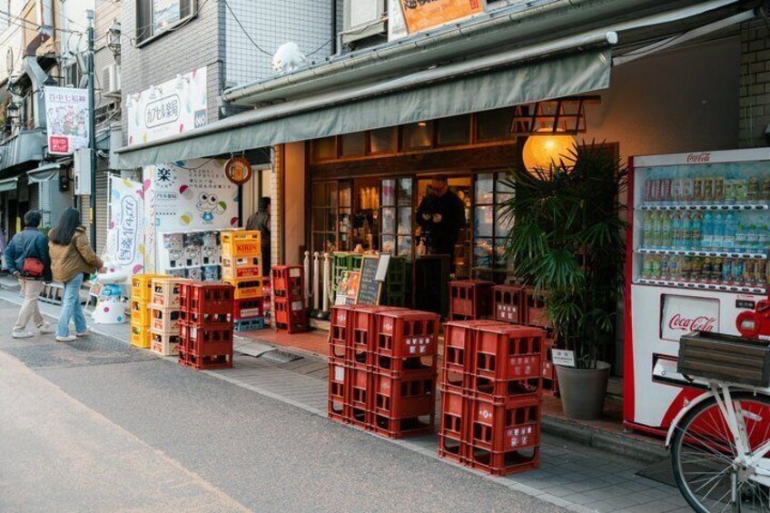 Een straat met kratten, een Coca-Cola automaat en een winkelgevel met een bord. 4