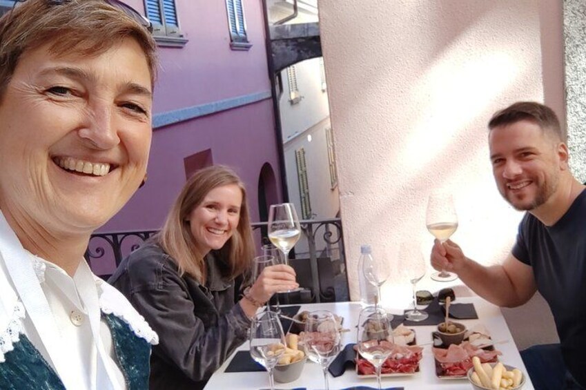 Une table avec de la nourriture et des verres à vin, une personne tenant un verre à vin, et un bâtiment en arrière-plan. 3