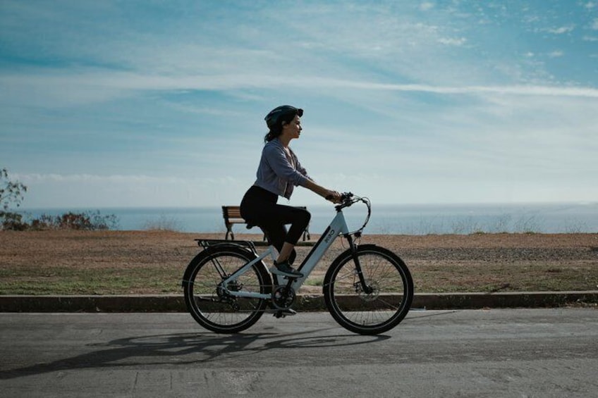 Une personne à vélo circule sur un chemin pavé, avec une zone herbeuse et une étendue d'eau en arrière-plan. 2