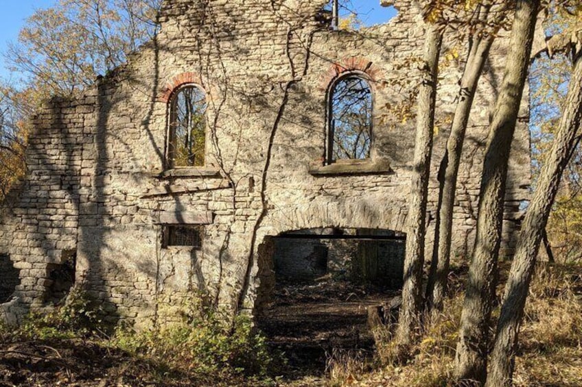 Un bâtiment en pierre abandonné, doté de fenêtres en arc de cercle et d’une grande porte béante, le tout entouré d’arbres. 3