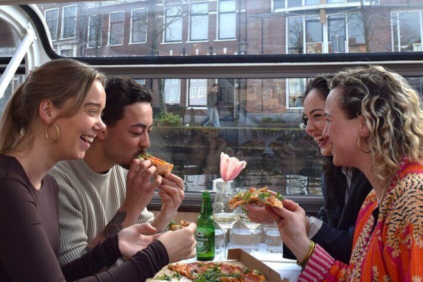 Four people sharing pizza and drinks at a table with a window view. 1