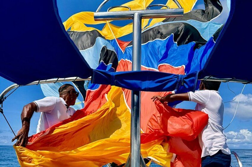 A sailboat with colorful sails, a person adjusting the sails, and a clear blue sky. 4