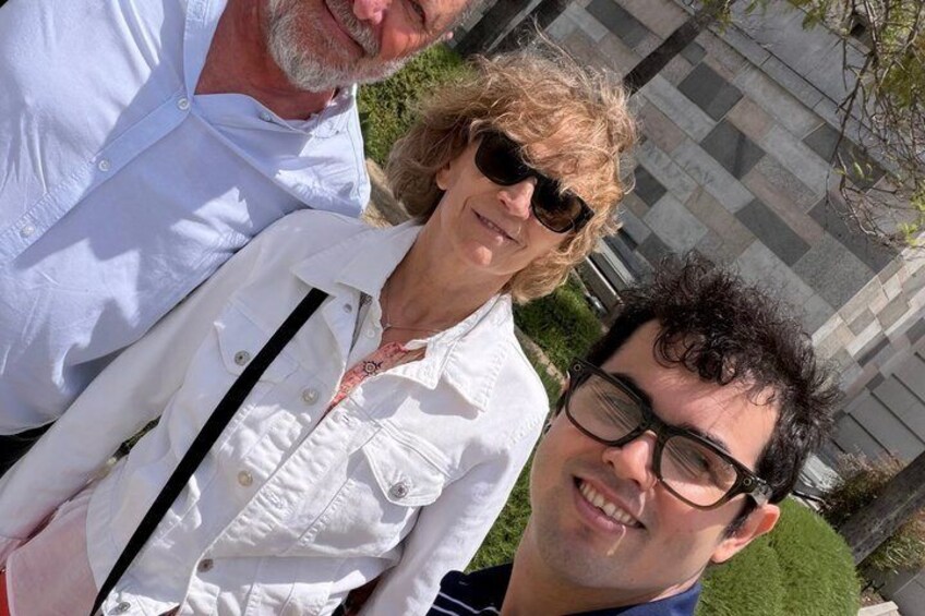 Three people standing outdoors with a building and greenery in the background. 2